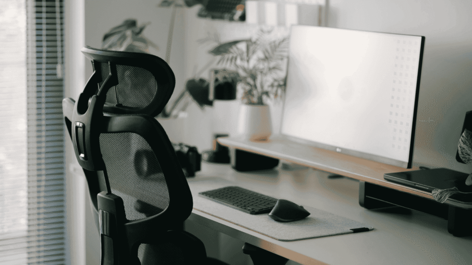 Ergonomic office chair at a clean desk with a large monitor, keyboard, and plants in the background.